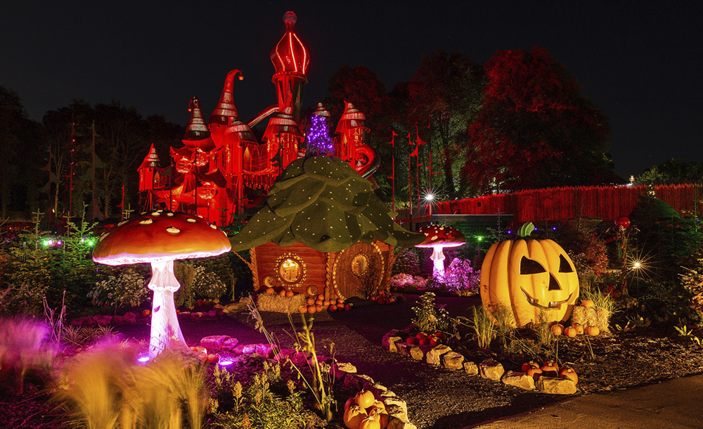 A giant mushroom, small playhouse, and pumpkin lit up at night with the large play structure in the background.