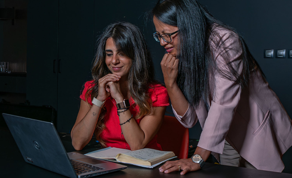 Two women smile as they look at a laptop computer screen.