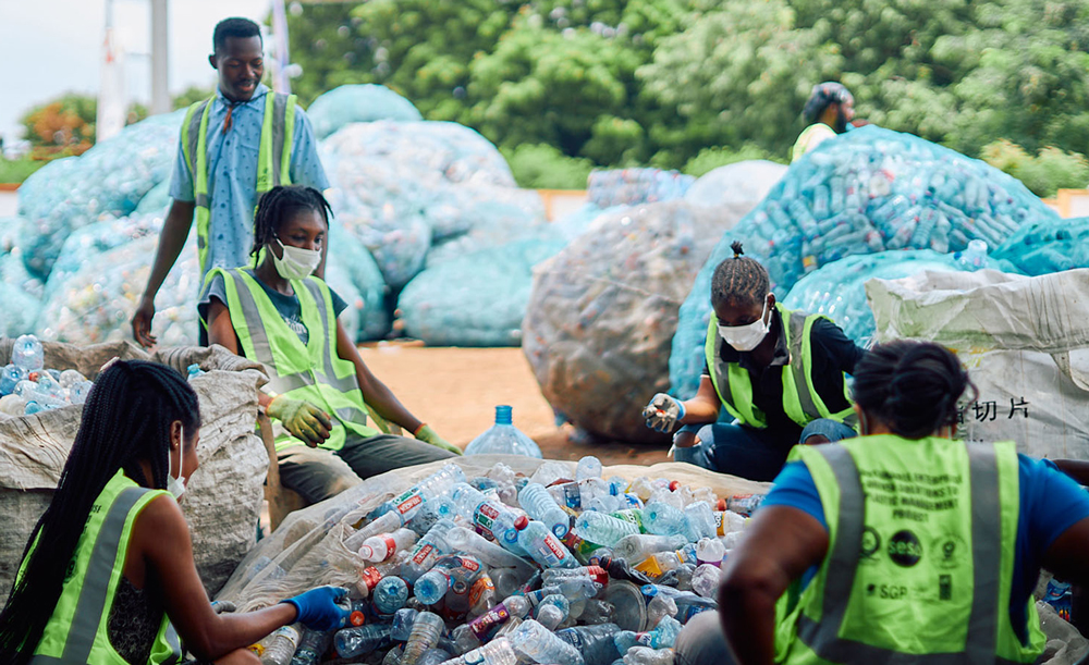 Five people put plastic bottles into a large plastic bag.