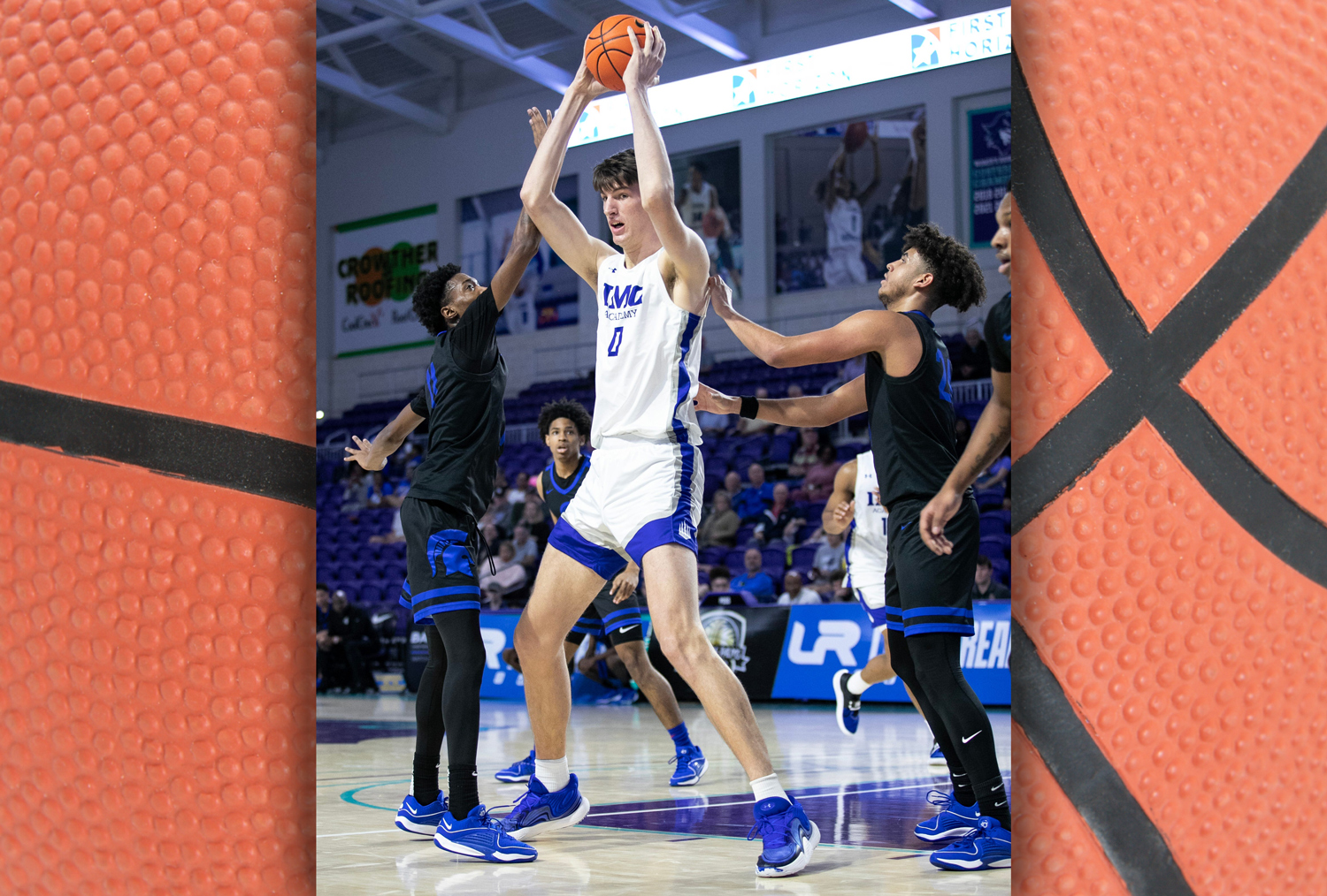 Olivier Rioux holds up a basketball as much shorter opposing players attempt to take it from him.