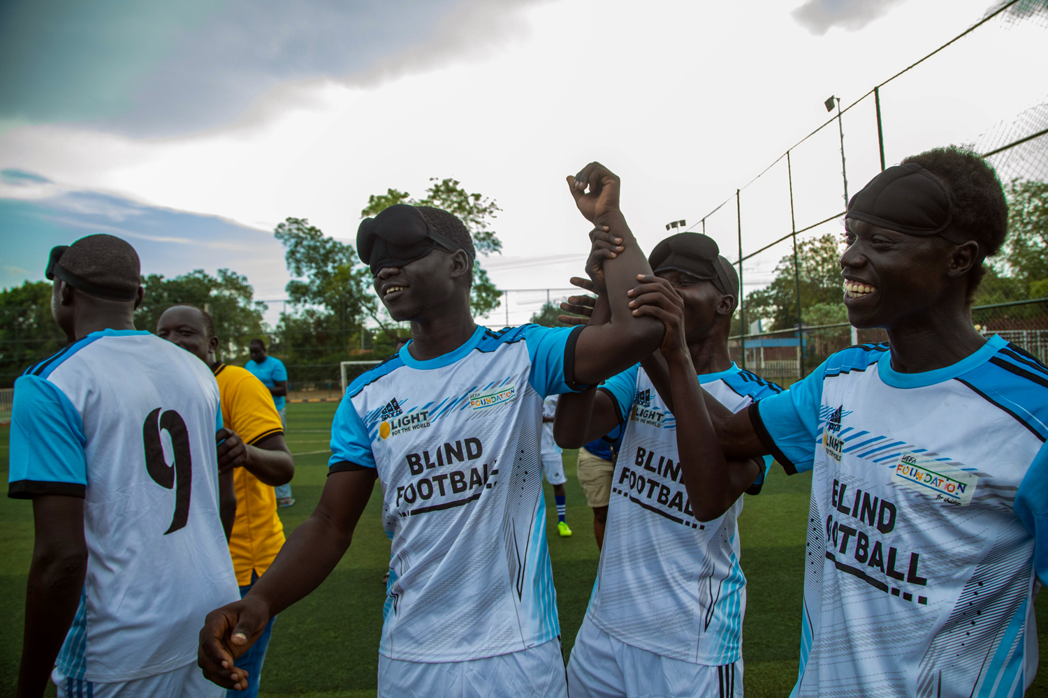 Three soccer players in uniform cheer and smile on the soccer field.