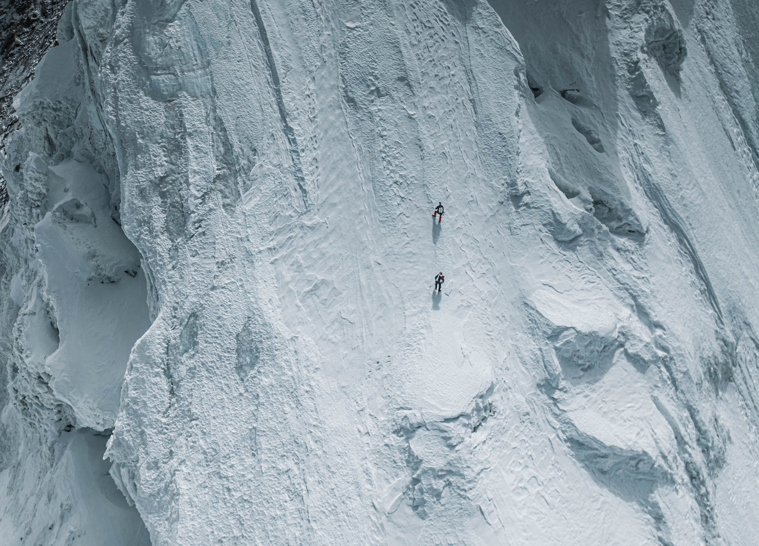 Two climbers look tiny on the face of a steep, snowy mountain