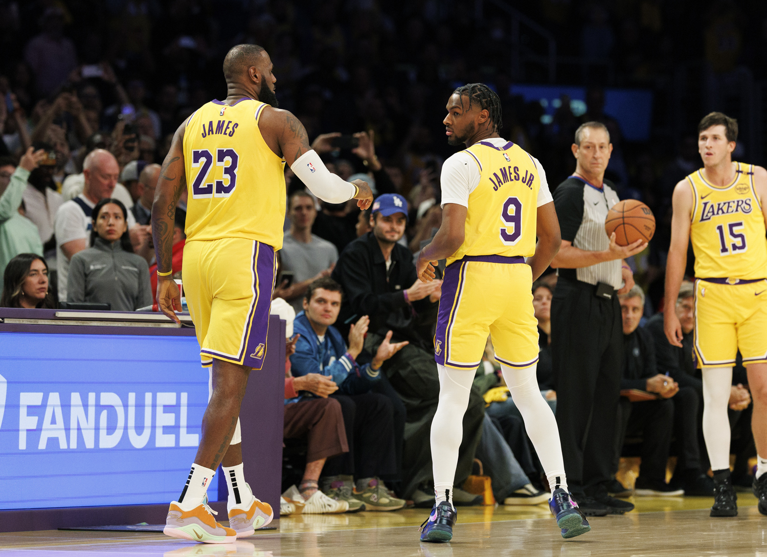 LeBron James and Bronny James face away from the camera as they stand on a basketball court in jerseys that read James and James Junior.