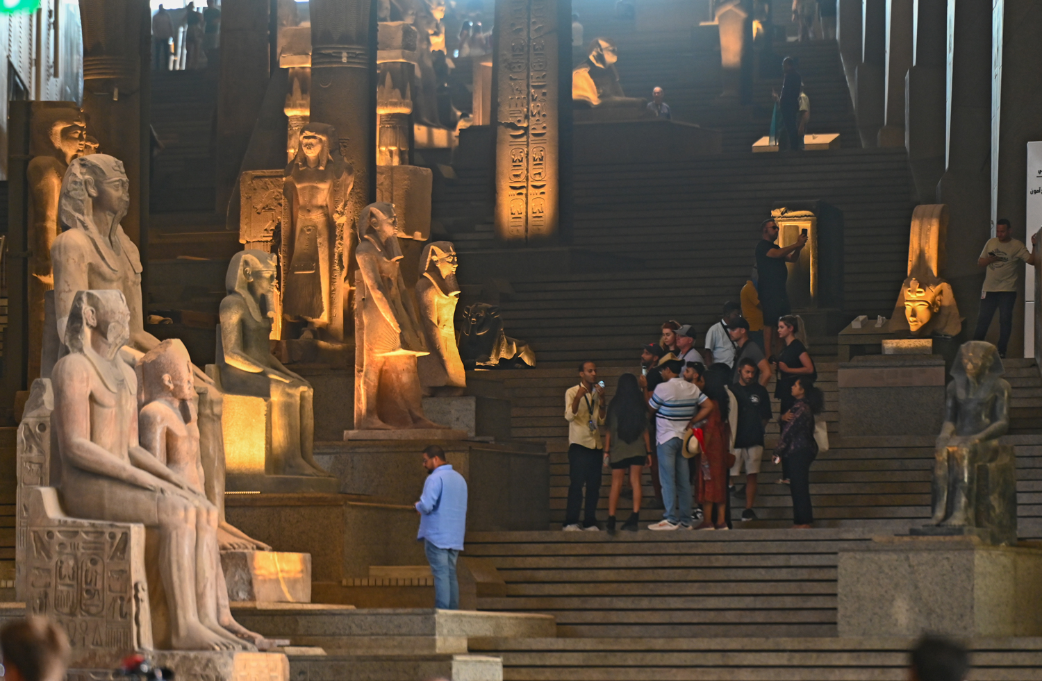 People stand on a large staircase that is lined with large sculptures of ancient Egyptian pharaohs.