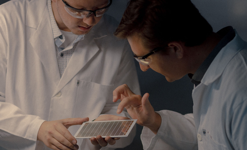 Two men in white labcoats examine a part of the ATS photovoltaic–thermal system.