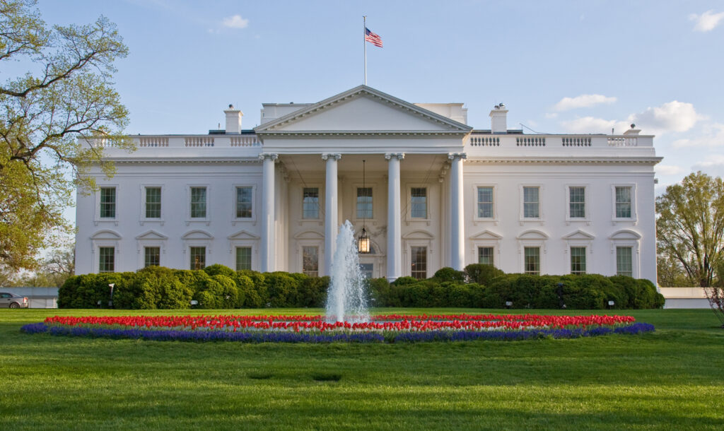 The exterior of the White House with flowers and a fountain in the foreground.