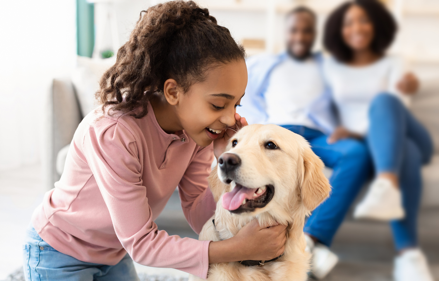 A child whispers in a dog’s ear as a smiling couple watches.