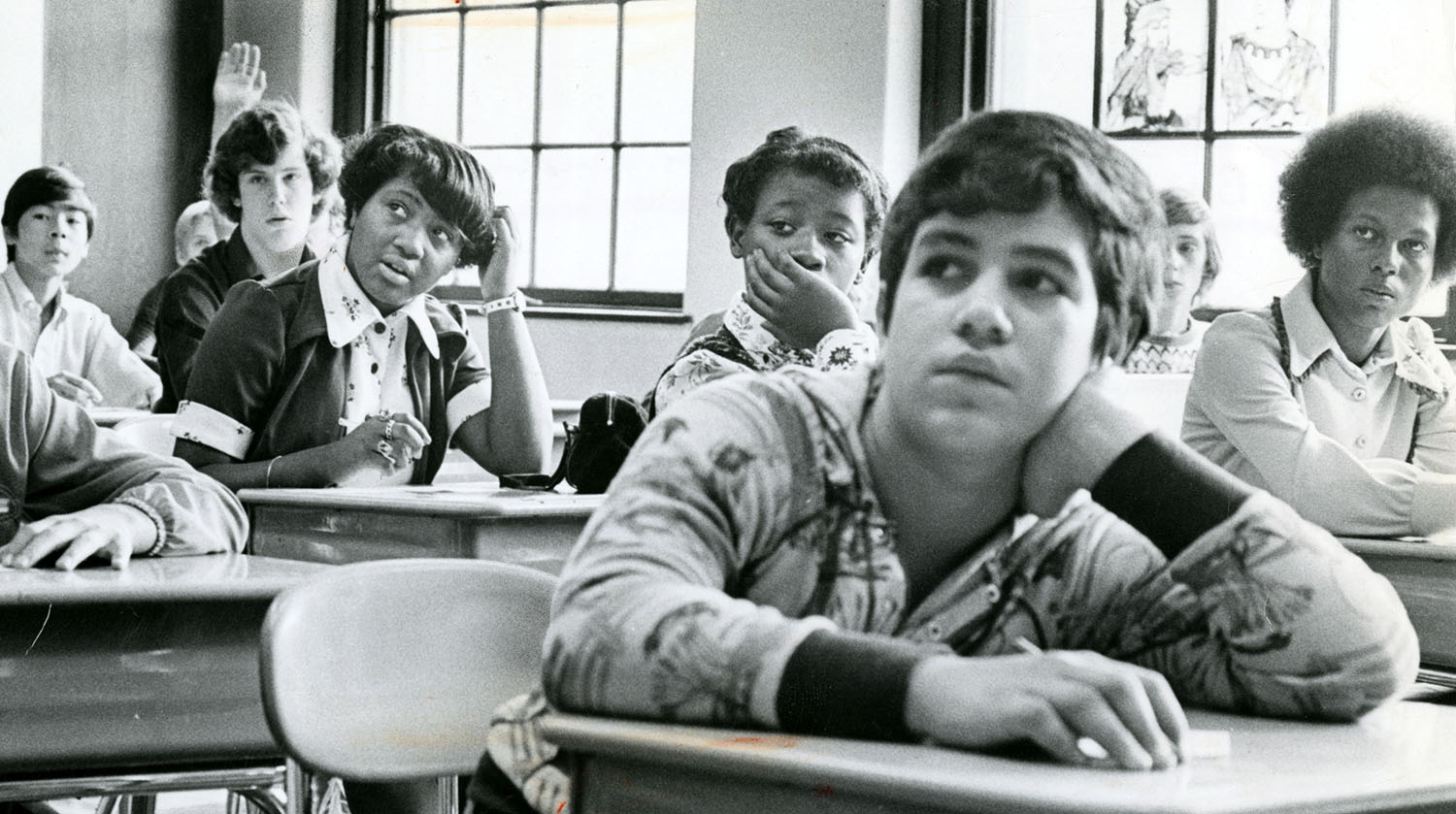 Middle school students of many races sit together in a classroom in 1974.