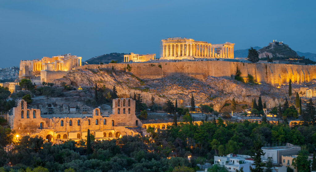 The Parthenon and other ancient buildings are lit up on a rocky outcrop in Athens, Greece.