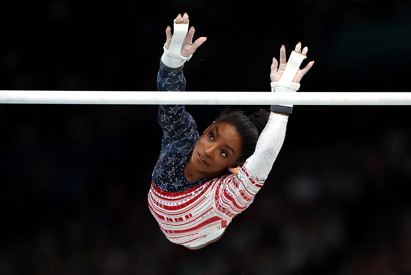 Simone Biles is in midair as she reaches for one of the uneven bars.