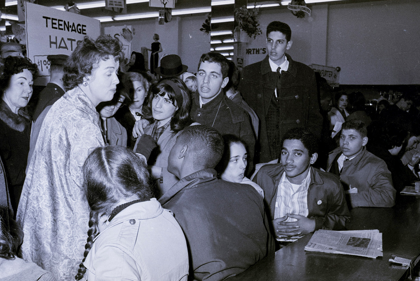 Many Black and white young people sit at the Woolworth counter as a white woman argues with them.