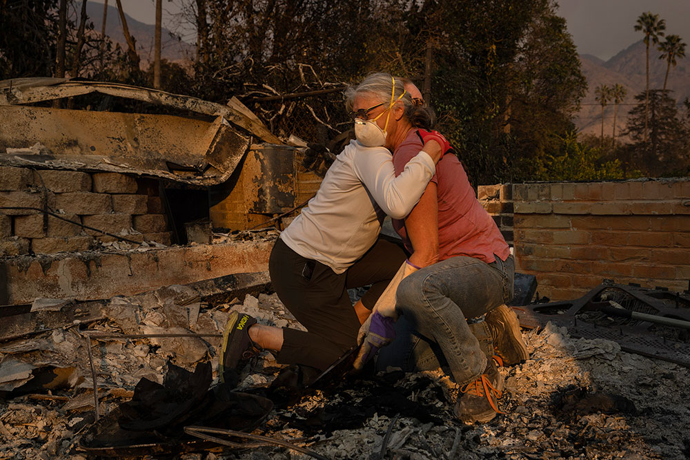 Two people hug and weep while kneeling in ruins from a fire.