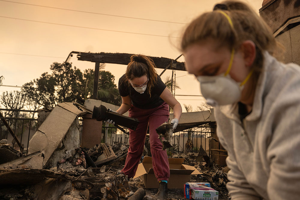 Two women wear respiratory masks as they sort through fire wreckage.