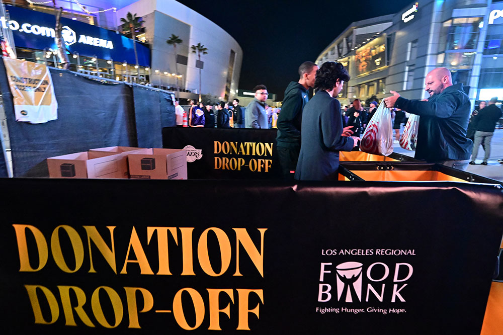 At a donation site outside a stadium, a man hands a full bag to a volunteer.