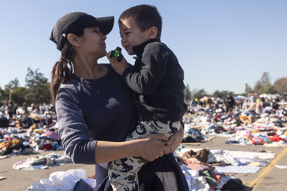 A woman holds a child and they smile at each other with donated clothing on offer in the background.