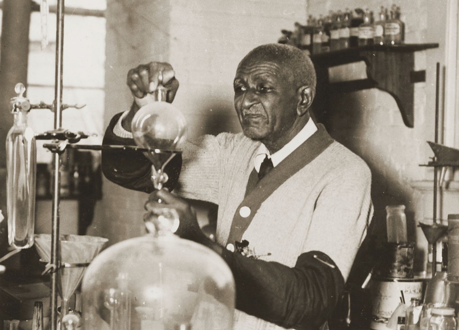 Older George Washington Carver works with chemistry equipment in his lab.