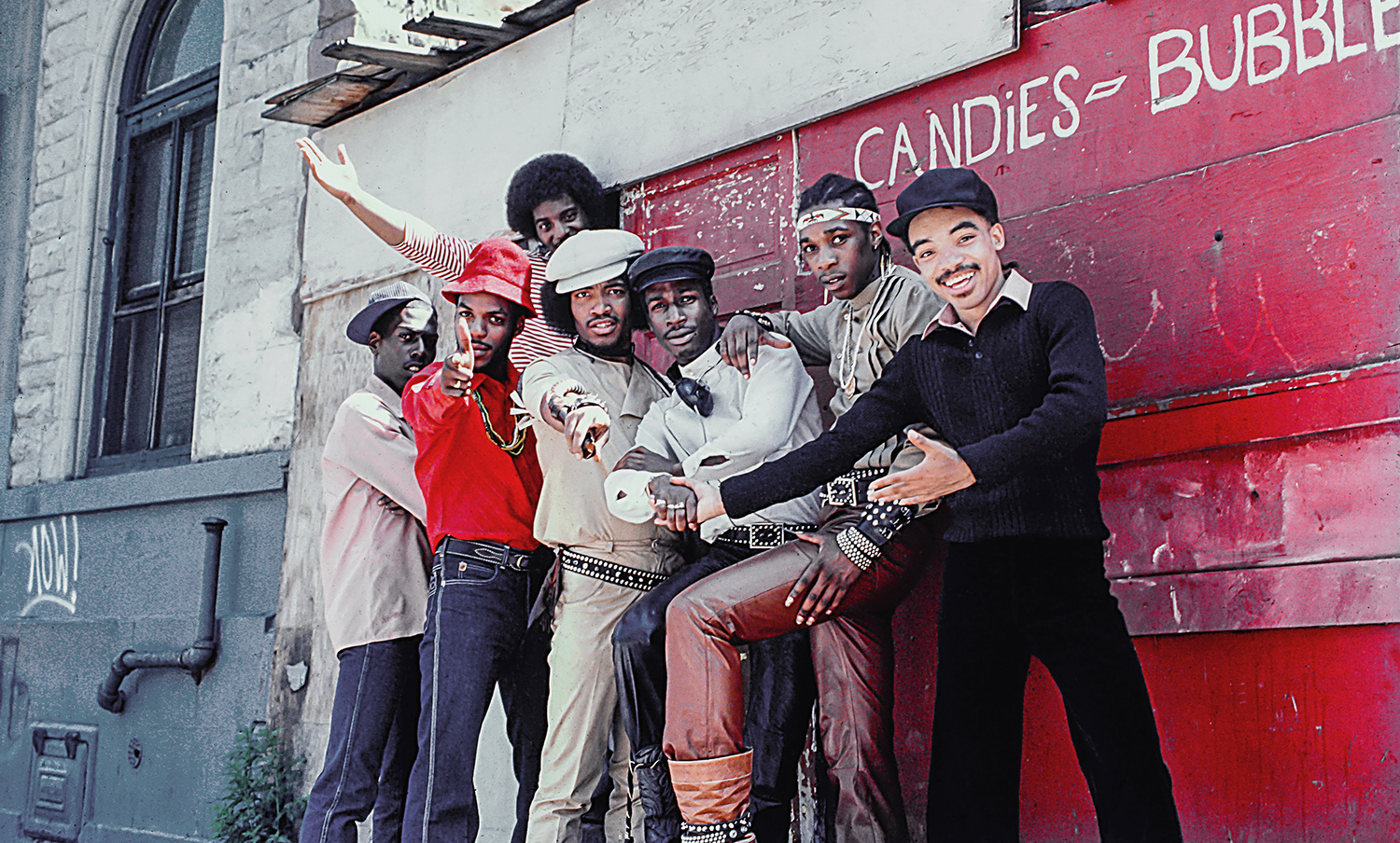 Seven members of Grandmaster Flash and the Furious Five pose in front of a wall in New York City.