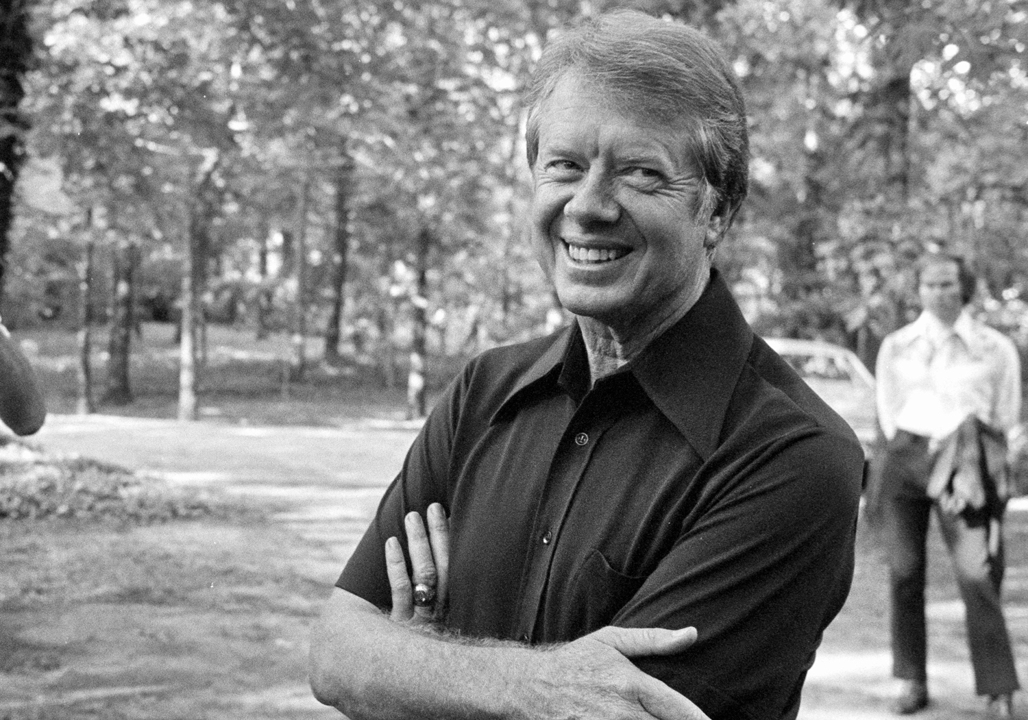 Jimmy Carter outdoors in casual clothing, smiling with his arms crossed.