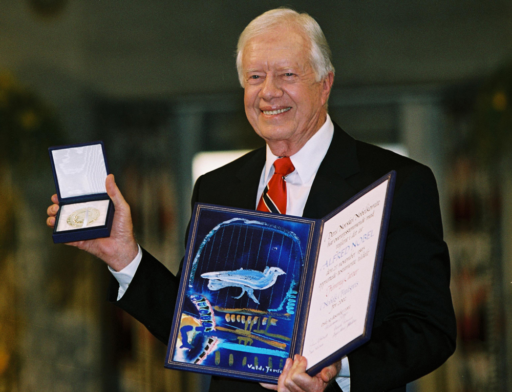 Jimmy Carter smiles and poses with a medal and a certificate he received when given the Nobel Prize.