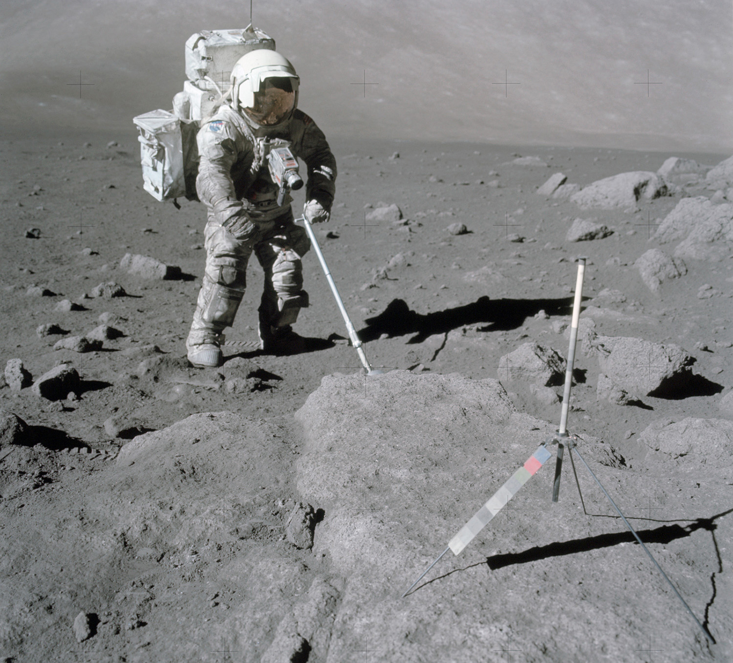 Astronaut Harrison Schmitt stands on the Moon and uses a tool to collect lunar samples.