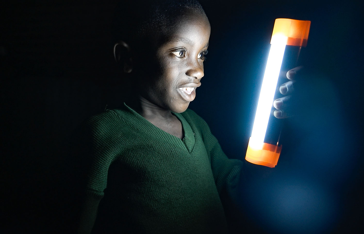 A child smiles while holding a solar-powered light in an otherwise dark room.