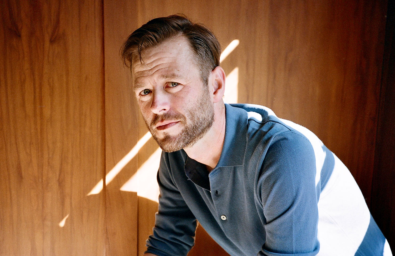 Press photo of Mac Barnett looking at the camera with a wood panel wall in the background.