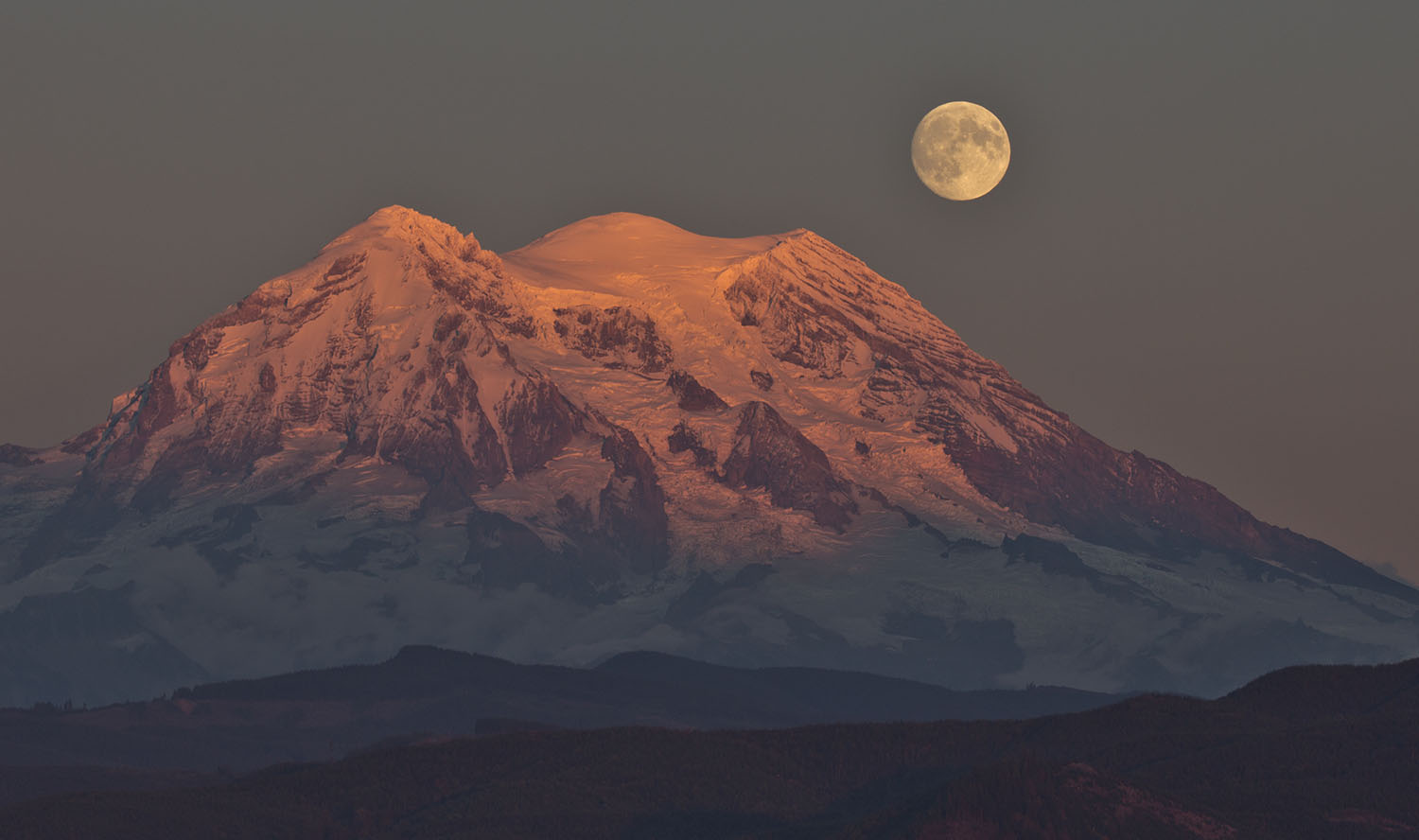 A full moon rises over snowy Mount Rainier.