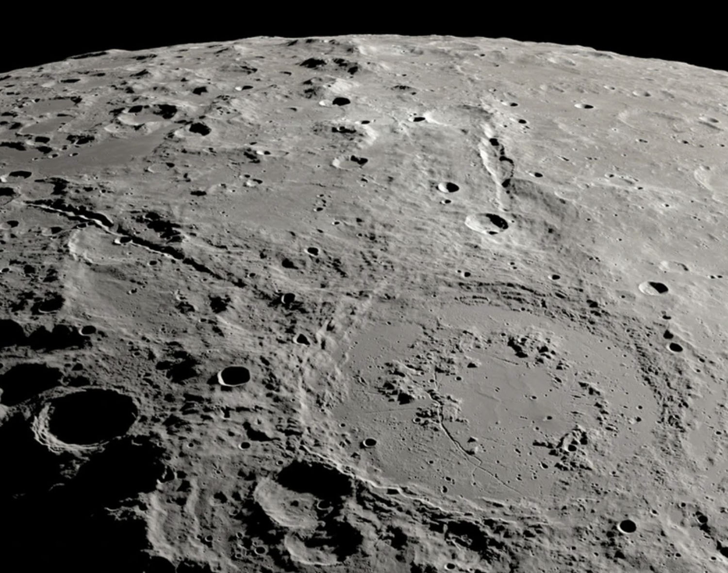 Two canyons radiate from a large crater on the Moon with many smaller craters nearby.