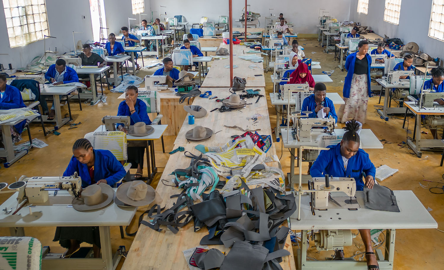 Several workers sit at sewing machines in a large room making Soma bags.