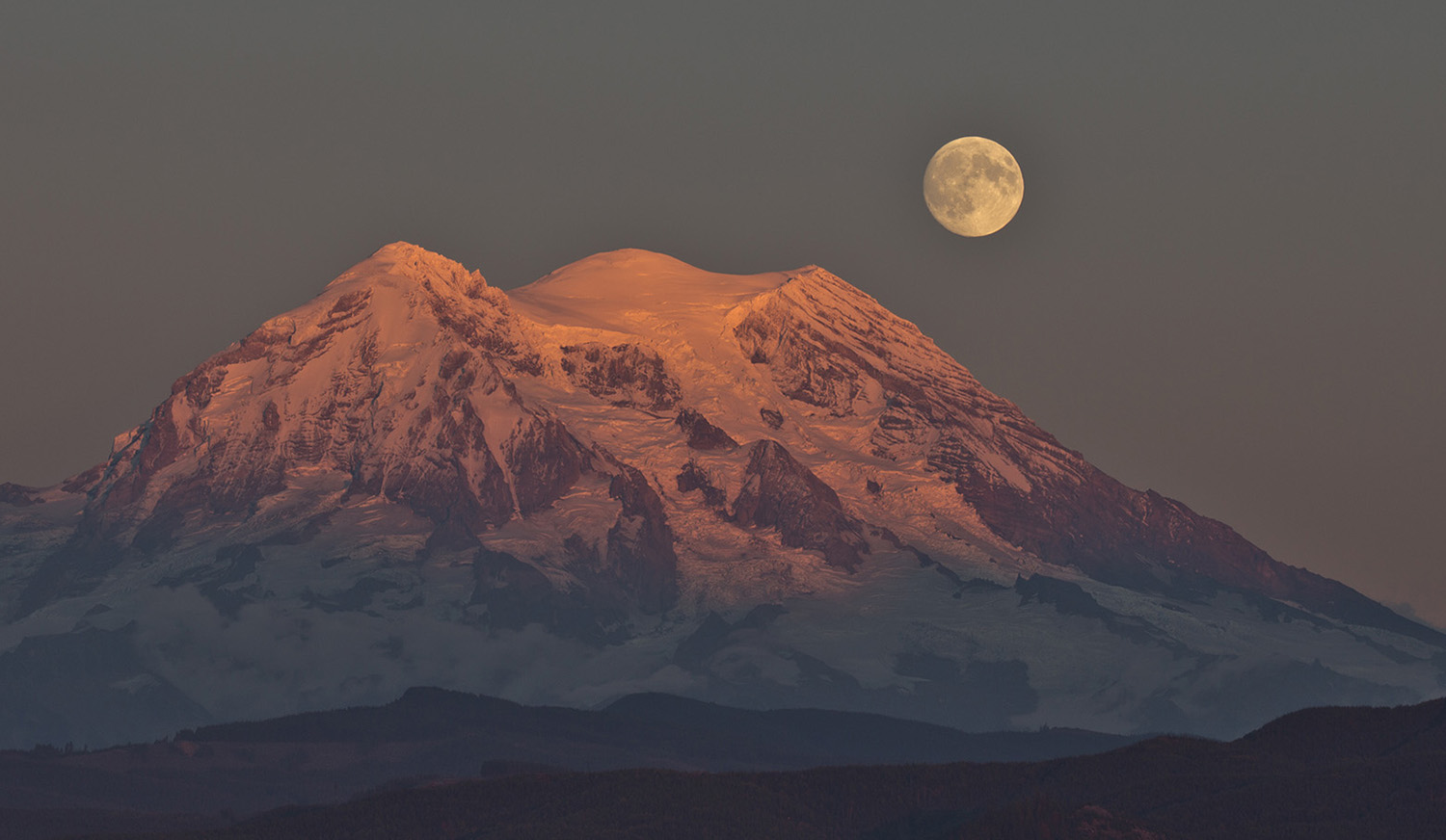 A full moon is over Mount Rainier at dusk.