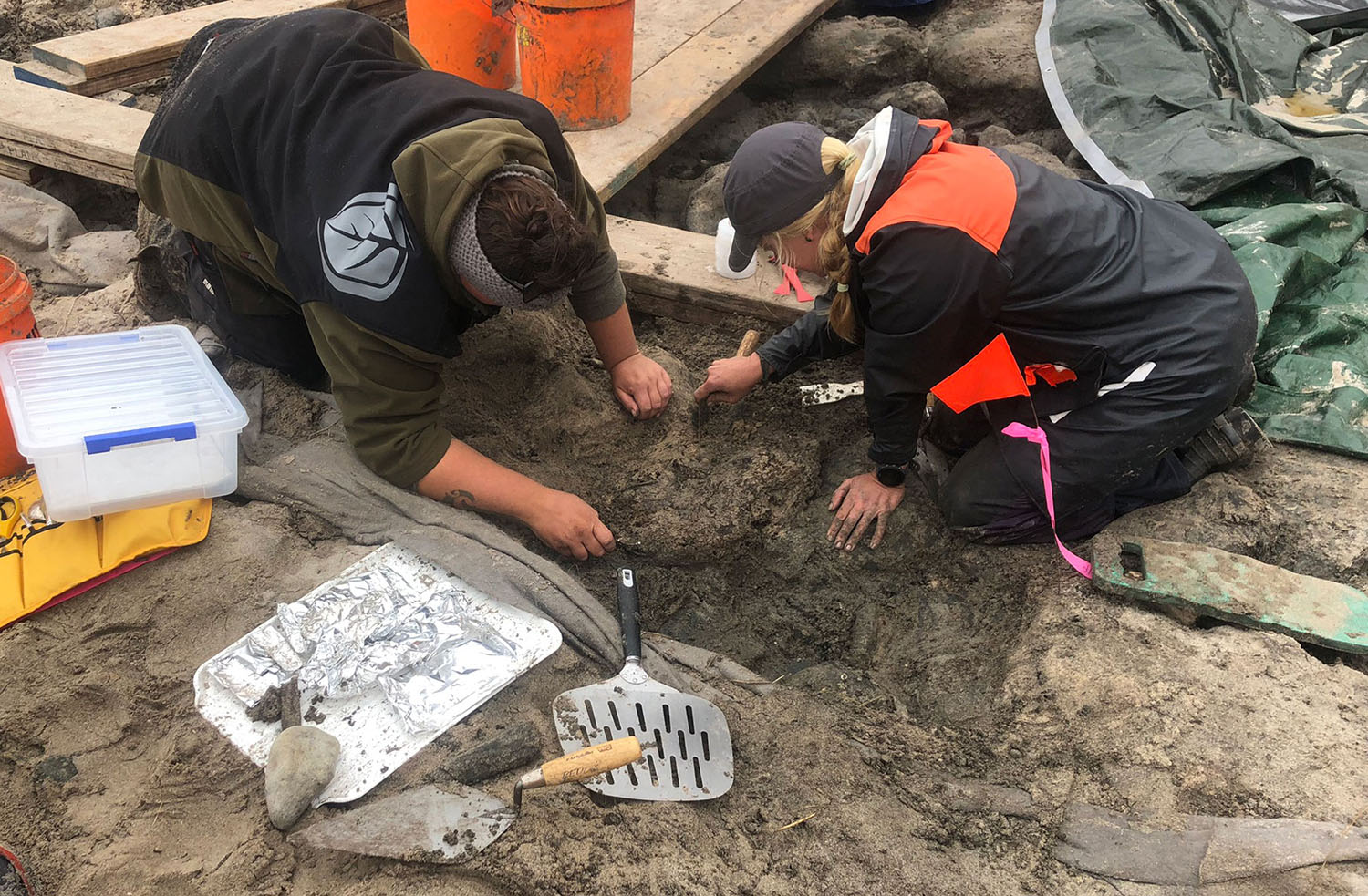 Two people use tools to excavate a site.