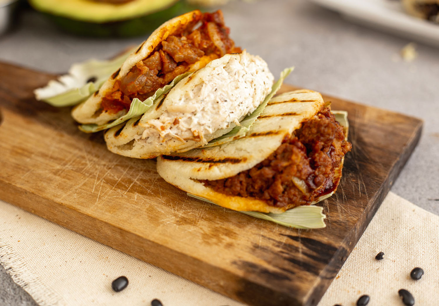 Three arepas containing different kinds of meat are arranged on a wooden board.
