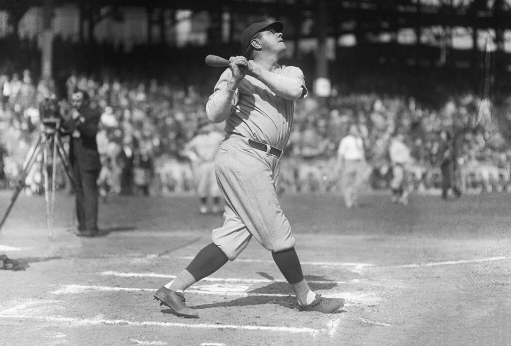 Babe Ruth stands at home plate and looks up with his bat over his right shoulder.