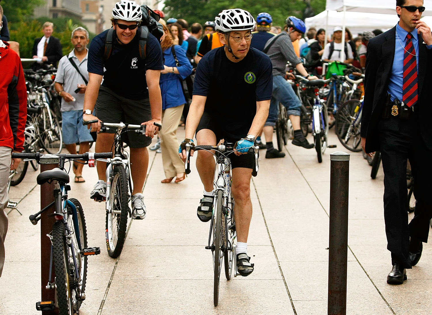 Secretary of Energy Stephen Chu and another man ride bicycles as other cyclists and pedestrians are behind them.