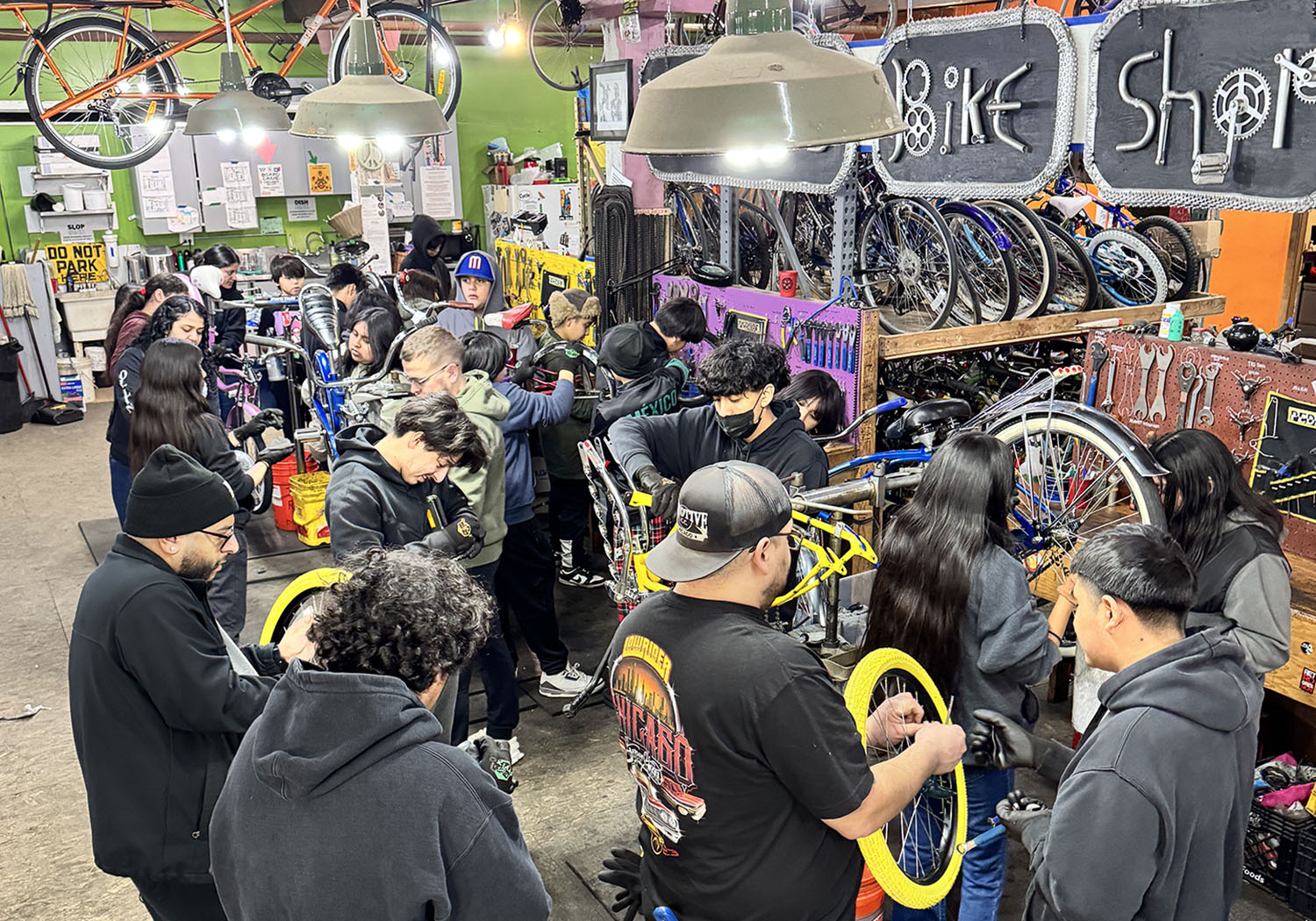 Several people are inside a bicycle shop repairing bicycles or holding bike parts.