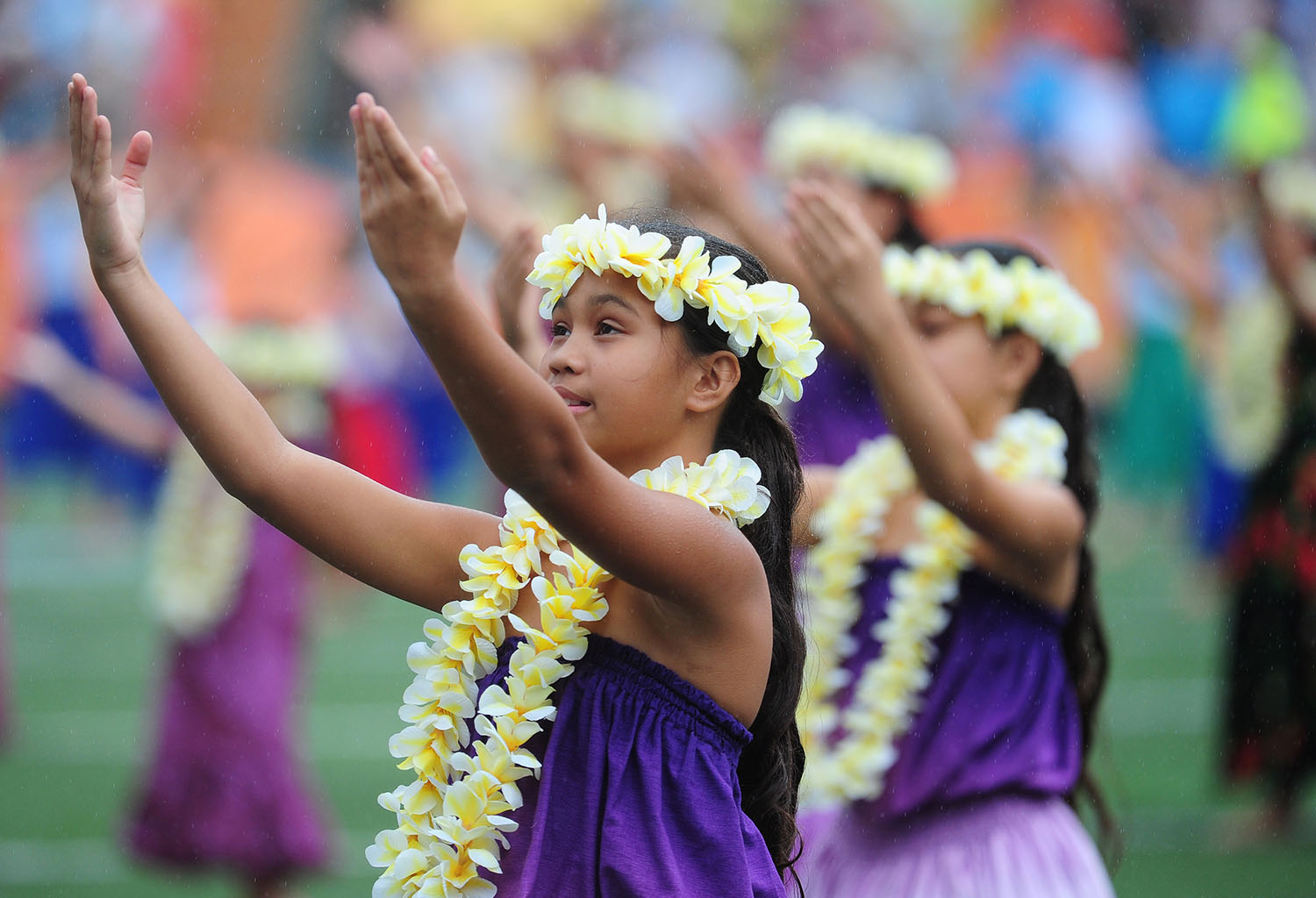 A young girl wearing traditional clothing lifts her arms as part of a hula dance.