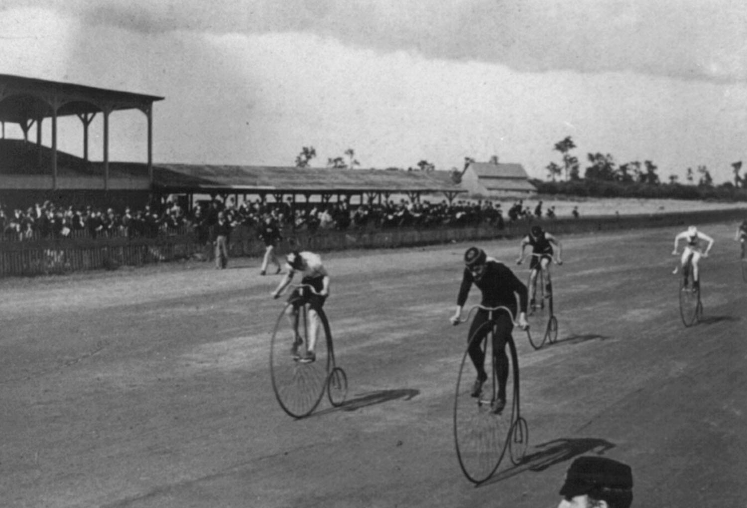 Several people ride ordinary bicycles on a racetrack as spectators watch.