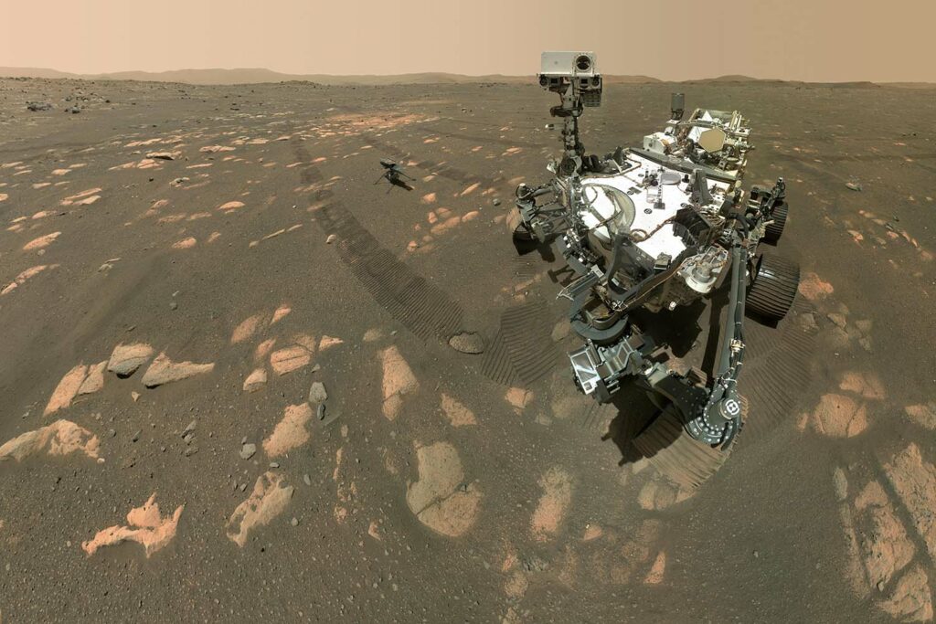 The Perseverance rover is on the Martian surface with hills in the background.