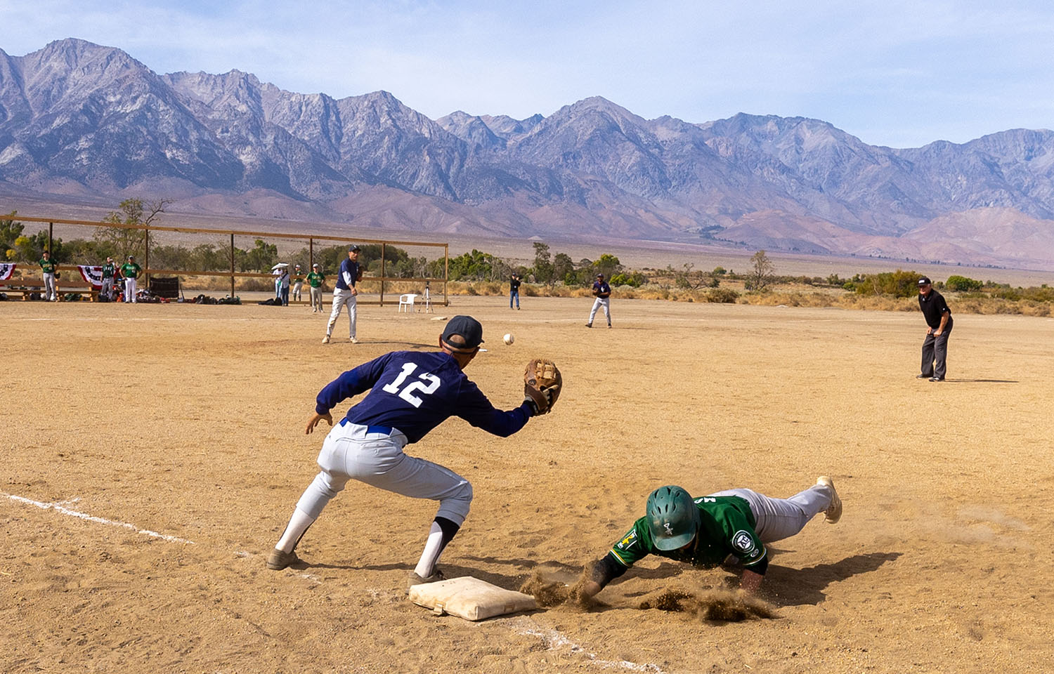 During a baseball game, a player dives into a base as the ball approaches the baseman’s glove.