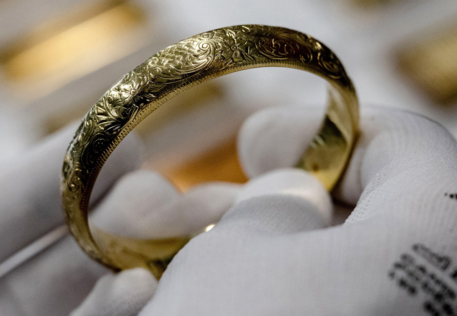 An engraved gold bracelet is held in two gloved hands.