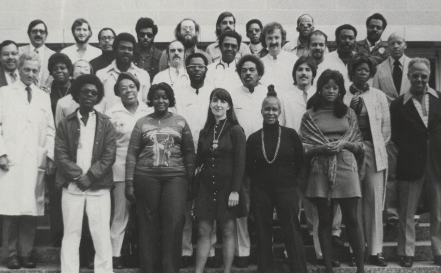 Men and women, some in street clothes and others in white coats, pose together for a photo.