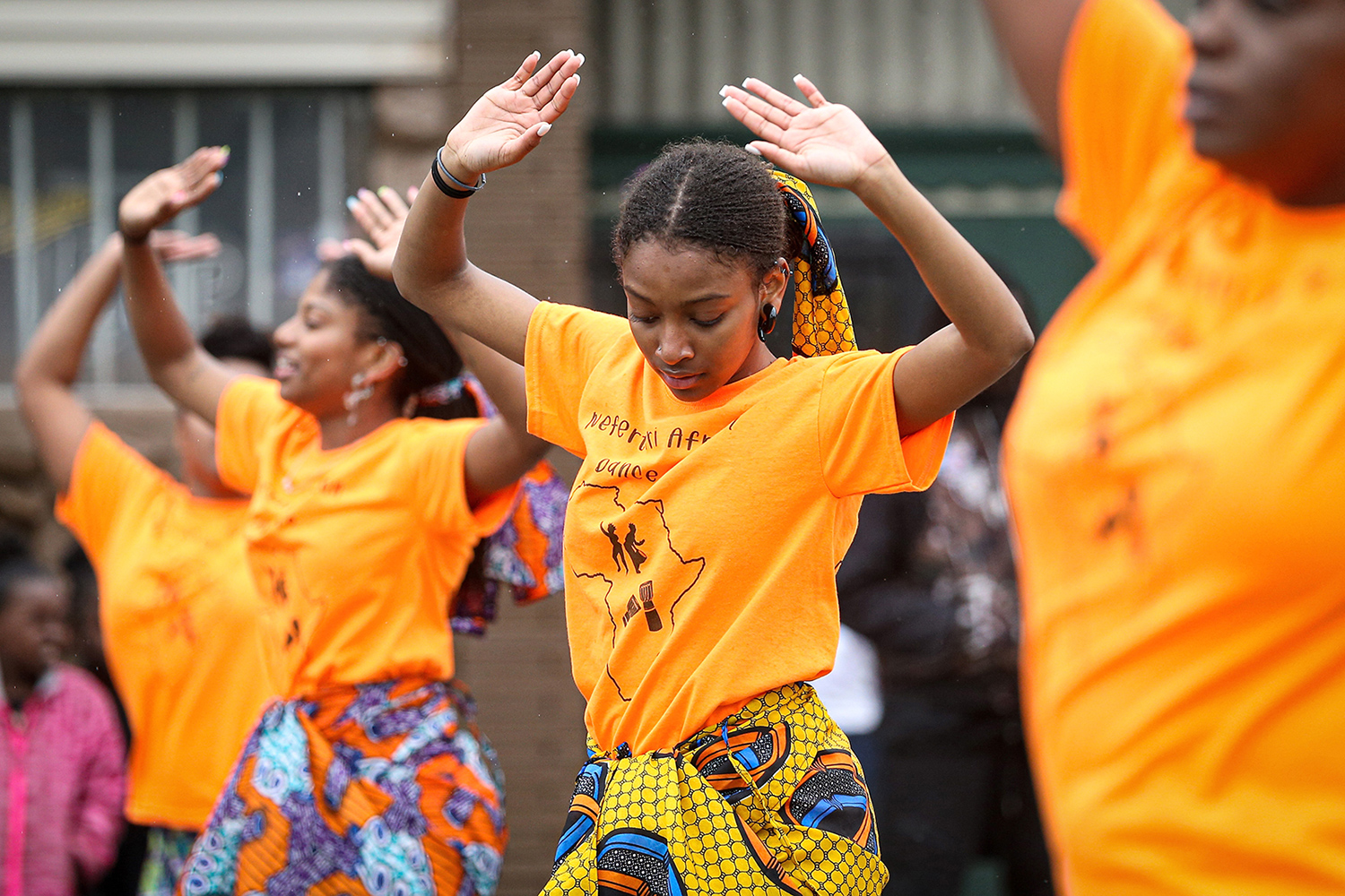 Young women wearing brightly colored clothing dance in a parade procession.