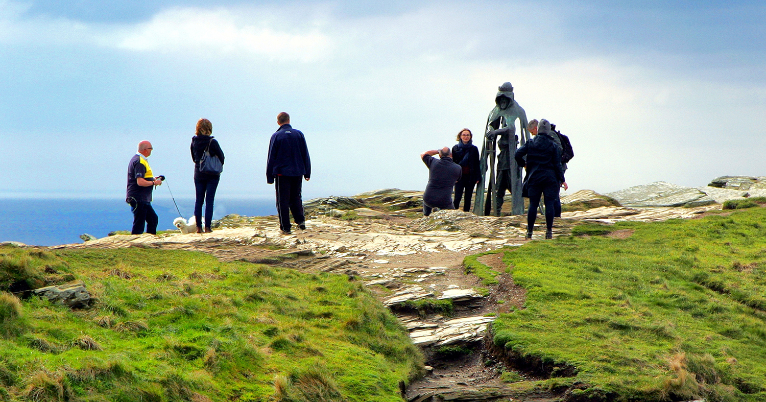 People pose for photos while standing next to a statue of King Arthur that is located in Cornwall, UK.
