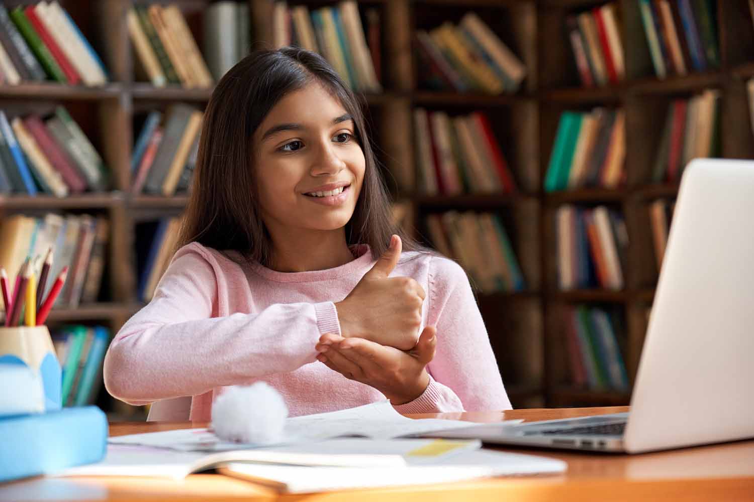 An elementary school-aged girl sits in front of a laptop computer smiling and using her hands in sign language.