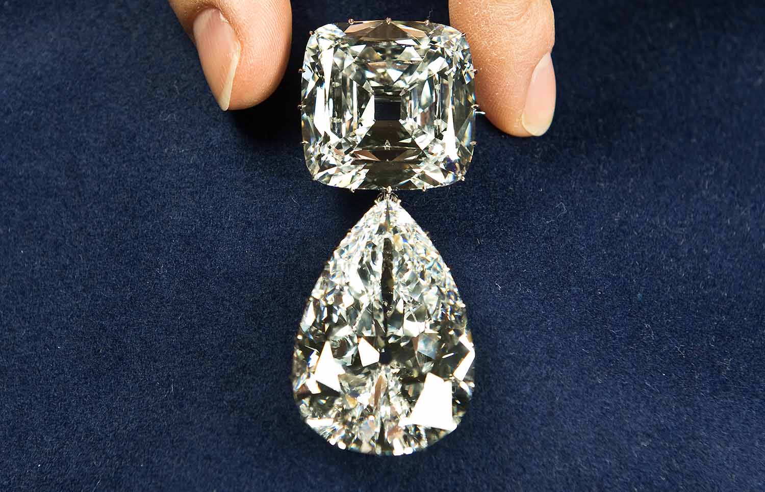A brooch made from the Cullinan diamond and featuring square and oval diamonds is held in two fingers.