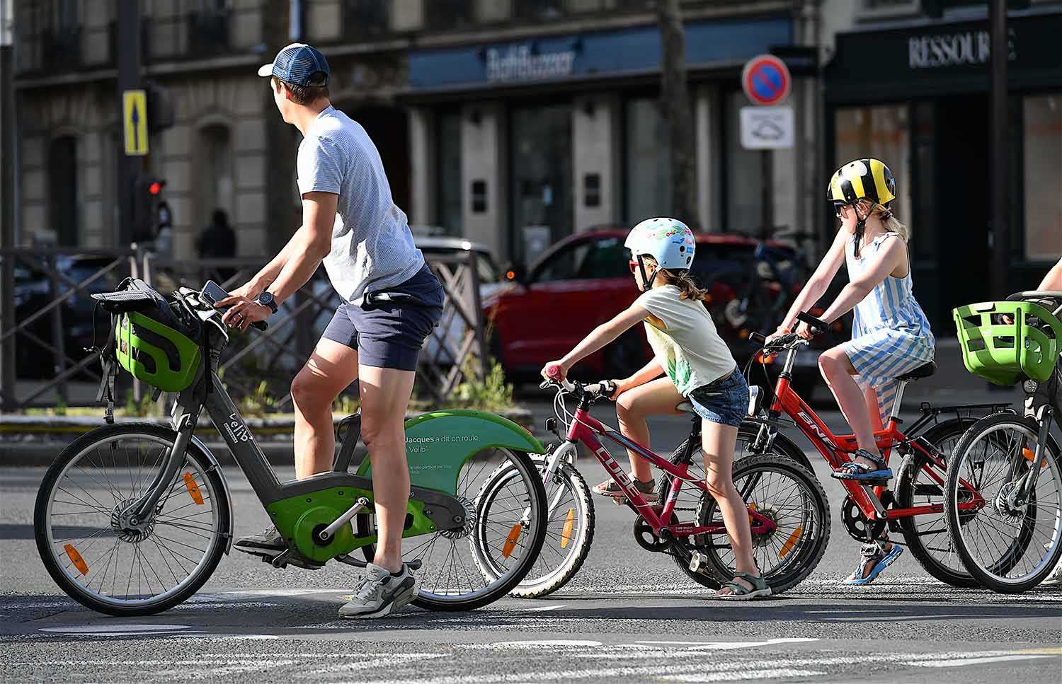 A man and two children wearing helmets ride bicycles on a Paris street.