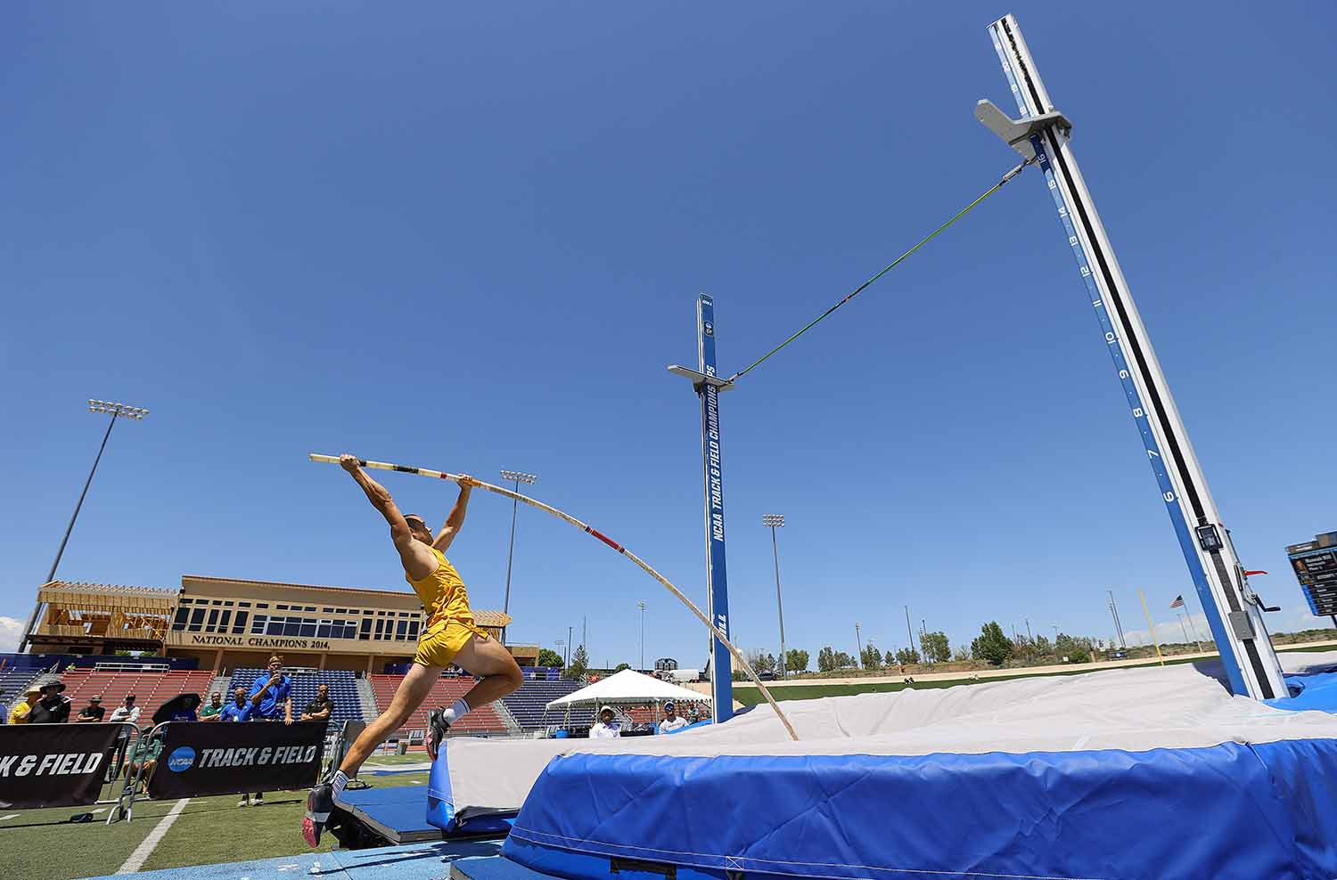 A man in an outdoor arena is about to launch himself over a bar using a pole.