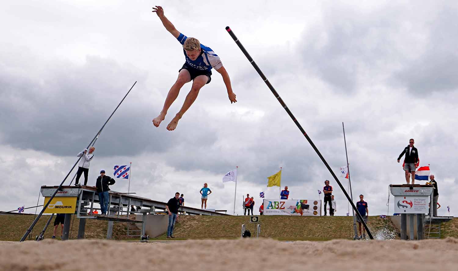 A man has jumped off a pole in a canal and is about to land in sand.