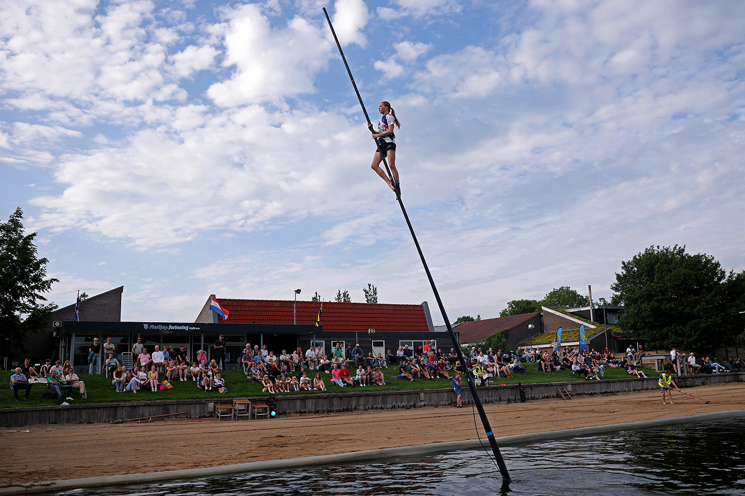 A woman is perched about two-thirds of the way up a pole that is sticking out of a canal.