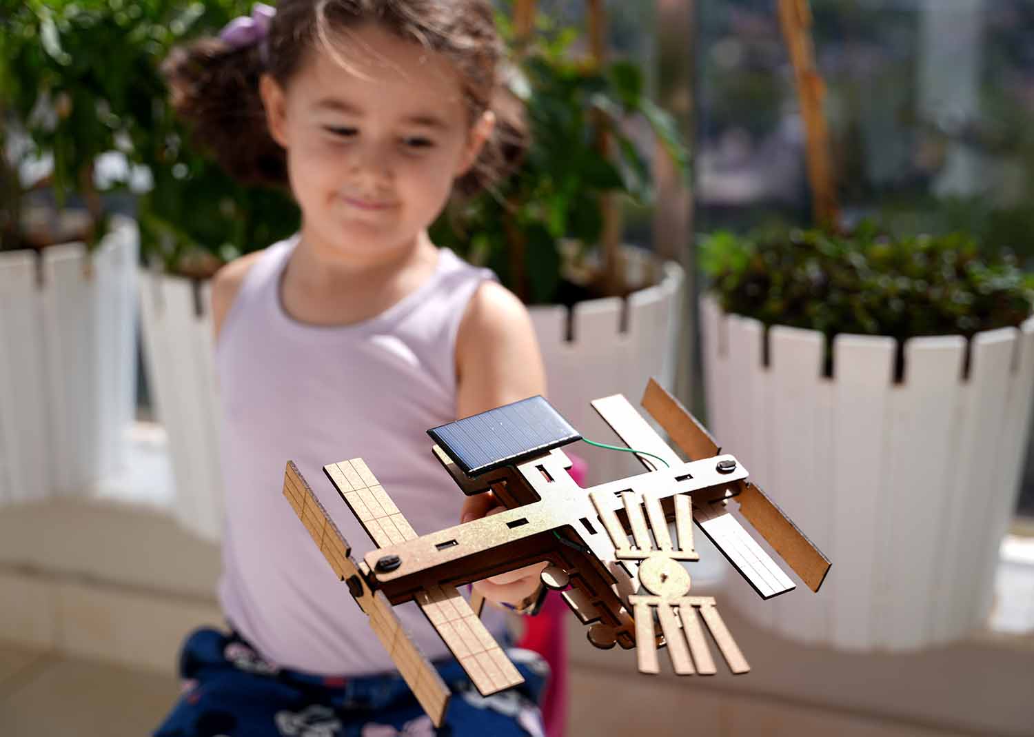 A child plays with a wooden space station toy that is powered by a small solar panel.
